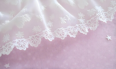 A delicate fabric with embroidered snowflakes and lace, set against a soft pink background.