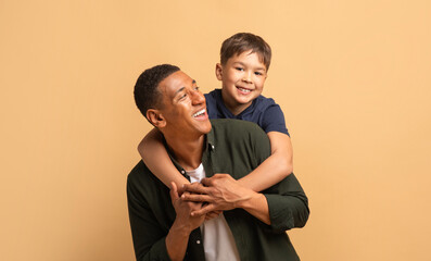 A father playfully embraces his son from behind, both sharing bright smiles. They showcase a strong...