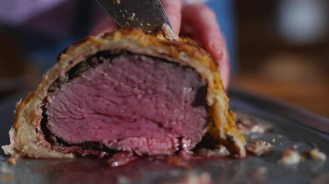 A person is cutting a piece of meat with a knife. The meat is cut in half and he is a roast