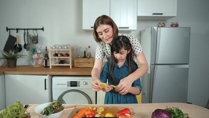 Smart caucasian mother and asian girl cooking together and chopping vegetable or preparing salad for dinner. Happy mom and daughter making healthy food with fresh food. Healthy food concept. Pedagogy.