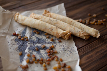 Rolled pancakes sprinkled with poppy seeds and raisins, placed on parchment paper over a rustic wooden table, creating a cozy and traditional dessert scene.