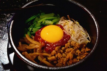 A bowl of bibimbap decorated with kimchi, egg yolk, and vegetables is a traditional Korean dish. Close-up photography