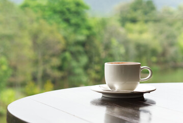 Hot coffee placed on a wooden table The background is blurred nature and trees.