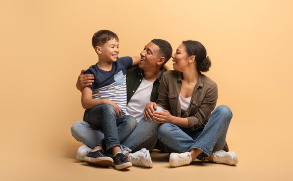 A loving African American family sits closely together, a father and mother enjoying quality time with their son. Smiles fill their faces as they embrace in a warm and inviting atmosphere.