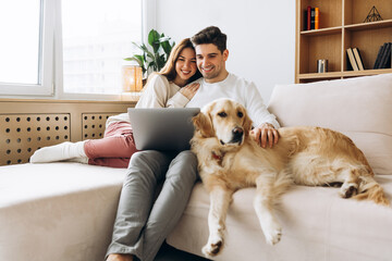 Happy couple relaxing on sofa with dog and laptop, enjoying streaming movie