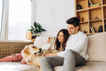 Happy couple relaxing on sofa with golden retriever dog at home