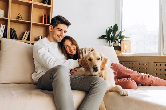 Happy couple relaxing on sofa with golden retriever dog at home