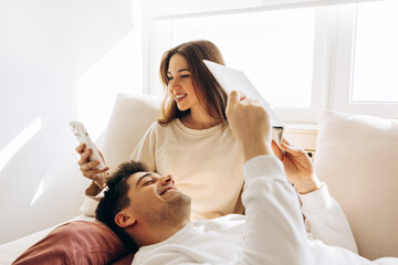 Obraz premium Happy couple relaxing on sofa, using tablet and smartphone