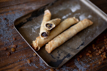 Rolled pancakes with sweet prune filling and poppy seed topping, served on a rustic baking tray, surrounded by raisins and powdered sugar on a wooden table.