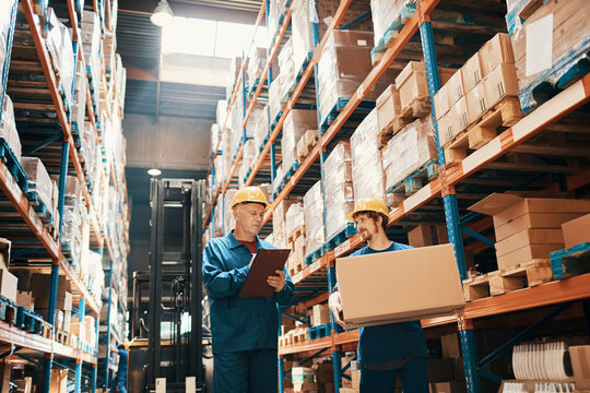 Warehouse workers in safety helmets managing inventory and carrying boxes in large storage facility