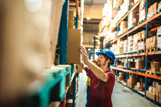 Male worker carrying box in large warehouse