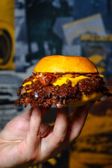 hand holding a doble smashed burger with bacon and onion
