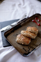 Three golden-brown homemade meat patties are placed on a vintage metal tray. The tray rests on a white tablecloth, with cutlery in the background, adding a rustic aesthetic to the composition.