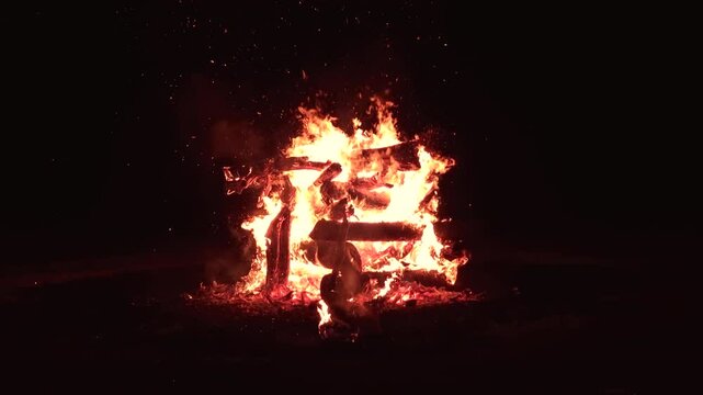 Bonfire made of logs burning with hot flames, with sparks flying. Bonfire isolated in the darkness with no people around.