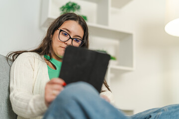 Young woman reading e-book on tablet at home, relaxing on sofa