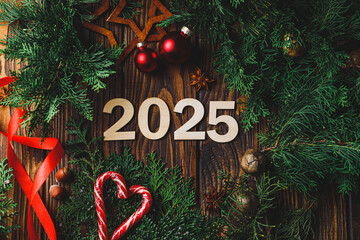 Wooden numbers 2025 on a wooden background surrounded by green branches of thuja and cypress