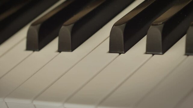 Close-up tracking shot of piano keys showing contrast and texture. Polished ebony and ivory piano clavier create a mesmerizing pattern of light and shadow, inviting a touch to create music