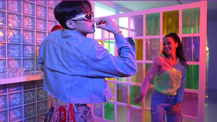 Asian man moving his arm while dancing with diverse team in neon light at night club. Happy dancer with stylish cloth moving along with multicultural hipster in lively mood at modern club. Regalement.