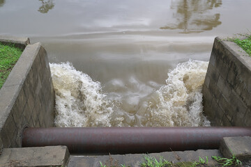 Floodwaters rush through a drain culvert, carrying fresh rainwater to the saltwater bay, creating a dynamic interplay of currents.