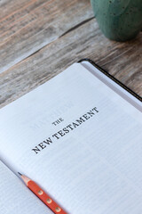 New Testament page in open holy bible book with coffee cup on wooden table. Close-up. Studying the gospel of God Jesus Christ, Christian biblical concept.