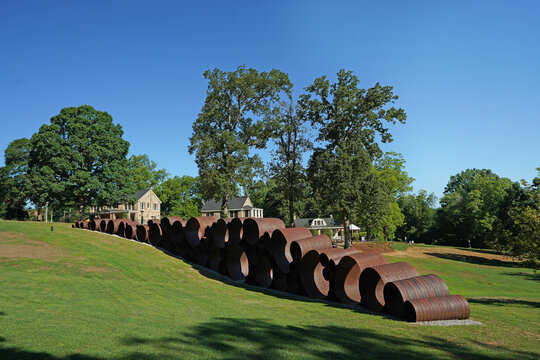 Raleigh, NC - USA - 5-30-2024:  The Attun sculpture by artist DeWitt Godfrey with the historic stone houses in the distance at Dix Park in downtown Raleigh