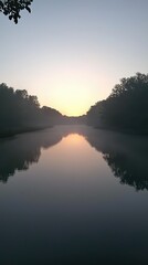 Fototapeta premium Serene Early Morning Reflection on Calm Water with Fog Rising in a Tranquil Forest Landscape at Dawn