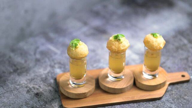Close up of Indian street food fuchka on a glass with sour spicy water.  Pani puri a chat item in India. 4K indian street food snacks.