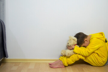 Little boy crying with her head down.The child is sitting sad scared on the floor in the corner and...