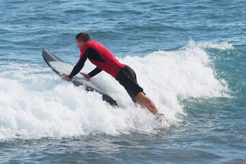 Surfer jumps in ocean with black surfboard.