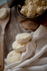 Raw cottage cheese pancakes (syrniki) with raisins, dusted with flour, arranged on a rustic wooden board alongside a dark wooden bowl filled with fresh cottage cheese. A cozy kitchen atmosphere 