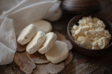 Raw cottage cheese pancakes (syrniki) with raisins, dusted with flour, arranged on a rustic wooden board alongside a dark wooden bowl filled with fresh cottage cheese. A cozy kitchen atmosphere 