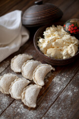 Fresh dumplings (varenyky) filled with cottage cheese, arranged on parchment paper alongside a bowl of cottage cheese and a white kitchen towel. The wooden background and flour-dusted details 