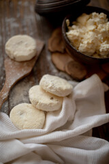 Round cottage cheese pancakes (syrniki) dusted with flour, placed on a wooden spoon and arranged next to a rustic linen kitchen towel. The warm, vintage-style kitchen background highlights a cozy atmo
