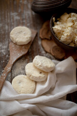 Round cottage cheese pancakes (syrniki) dusted with flour, placed on a wooden spoon and arranged next to a rustic linen kitchen towel. The warm, vintage-style kitchen background highlights a cozy atmo