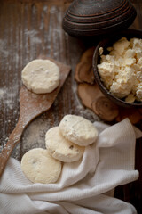 Round cottage cheese pancakes (syrniki) dusted with flour, placed on a wooden spoon and arranged next to a rustic linen kitchen towel. The warm, vintage-style kitchen background highlights a cozy atmo