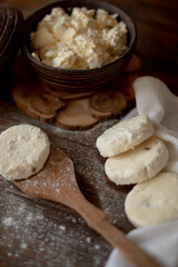 Round cottage cheese pancakes (syrniki) dusted with flour, placed on a wooden spoon and arranged next to a rustic linen kitchen towel. The warm, vintage-style kitchen background highlights a cozy atmo