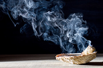 a smudging ritual with a shell containing burning sage or palo santo, emitting thick, swirling...