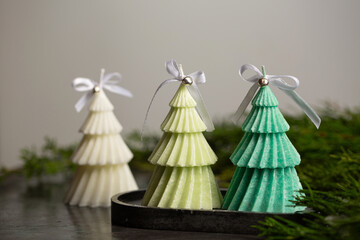 Three scented Christmas candles in the shape of Christmas trees with bows and small bells on a black plaster stand