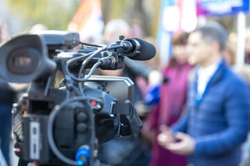Professional video camera capturing an outdoor media interview with blurred people in the background