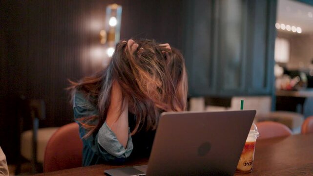 Frustrated and Overwhelmed. A young woman runs her hands through her hair, overwhelmed by the pressures of work, staring at her laptop in a moment of frustration.  