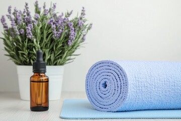 Rolled yoga mat, essential oil bottle and lavender plant creating relaxing atmosphere