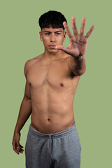 Serious latino man showing stop sign with hand on green background