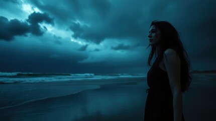 Woman stands on a beach at night, looking out at the ocean
