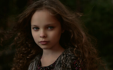 Portrait of little cute smiling girl  with long curly hair in stylish retro coat walking in the garden or park.