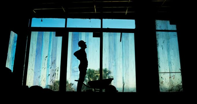 Man, injury or back pain on construction site for building, fatigue or wheelbarrow in silhouette. Worker, tools or tired at worksite for overworked, accident or stretching for muscle relief in shadow