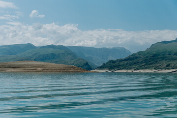 Landscape of blue deep lake in light of sun in daytime, clouds in sky, mountains