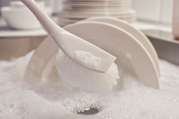 Dishwashing brush with soapy foam. Kitchen sink filled with water and detergent. Washing dishes.