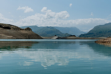 Landscape of blue deep lake in light of sun in daytime, clouds in sky, mountains