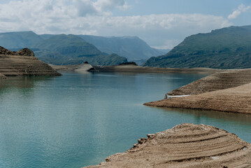 Landscape of blue deep lake in light of sun in daytime, clouds in sky, mountains
