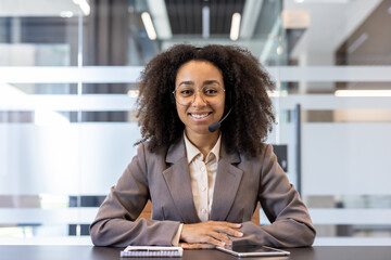 Portrait of a young smiling African American woman sitting behind a desk in a headset and looking...